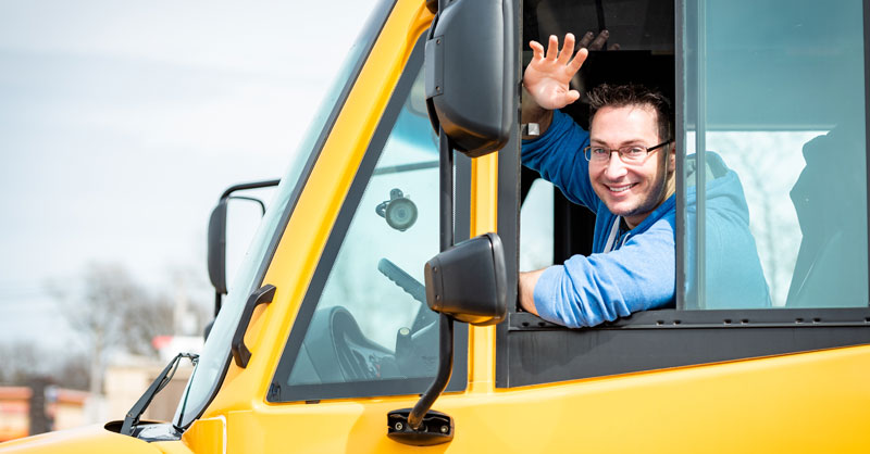Male school bus driver waving out of bus window