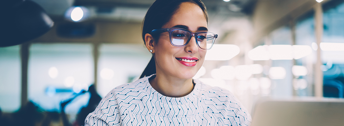 Woman wearing glasses and red lipstick smiling while watching laptop screen