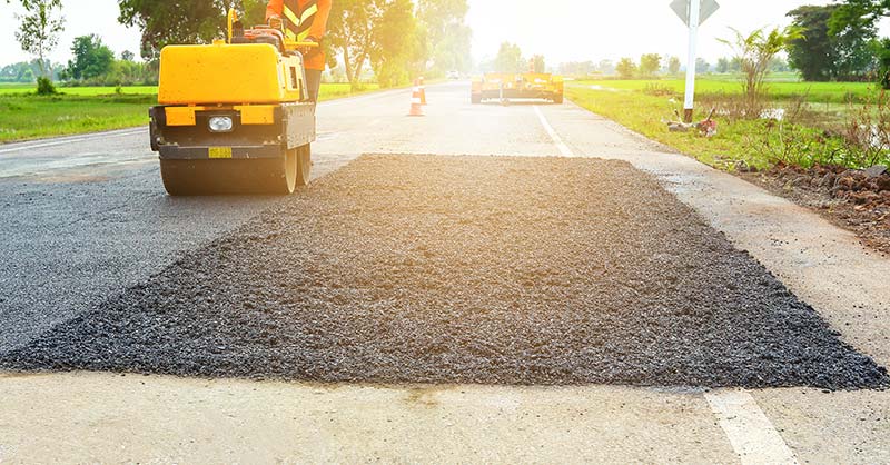photo of asphalt roller truck next to asphalt patch on road