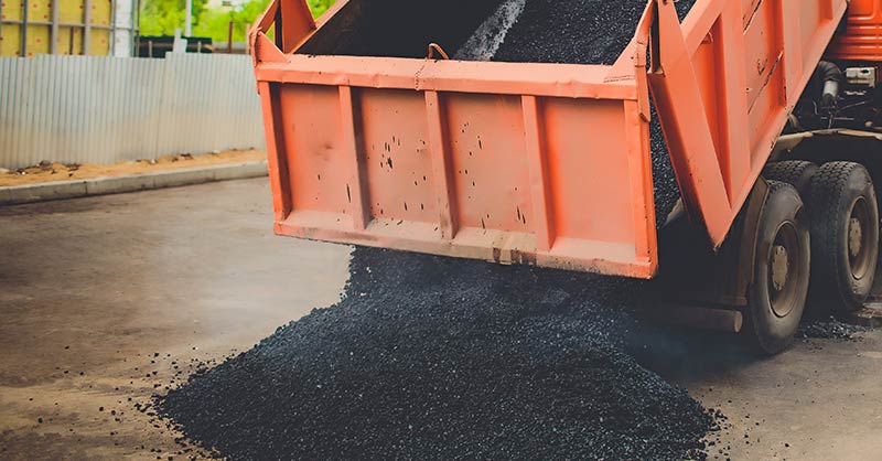 photo of orange dump truck unloading asphalt